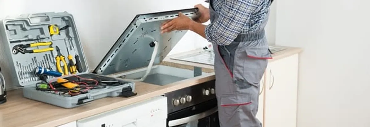 Cooktop repair technician lifting a built-in stovetop for service in Colorado Springs, CO