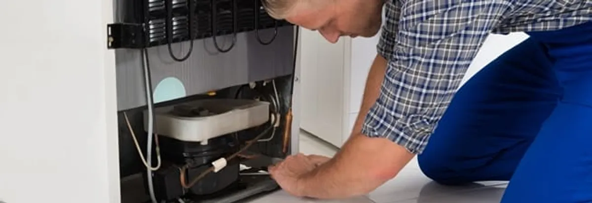 Refrigerator repair technician servicing the compressor and condenser area in Colorado Springs, CO